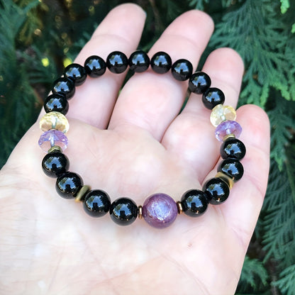 Black bead bracelet held in hand, showing purple center cabochon and gold spacers