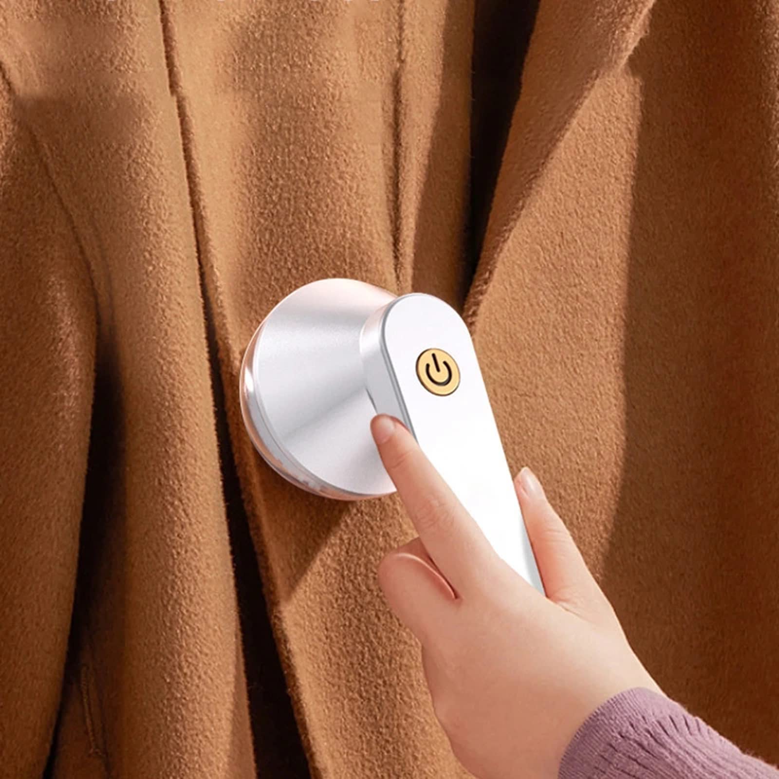 Rechargeable lint remover head on beige fabric, finger pressing power button