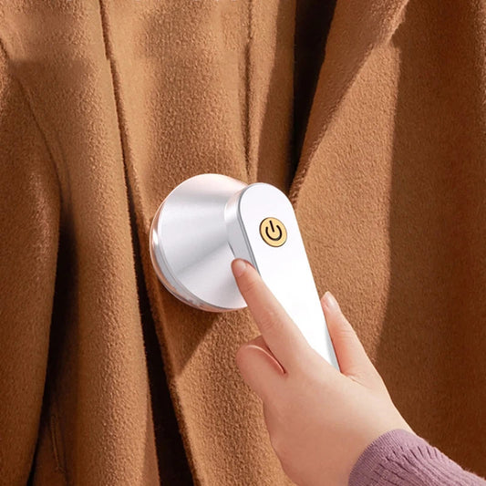 Rechargeable lint remover head on beige fabric, finger pressing power button